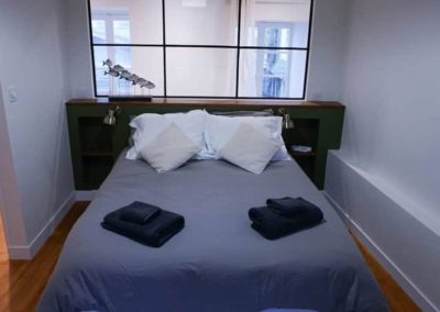 Lit double avec linge gris et coussins blancs dans une chambre épurée