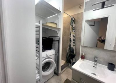 Salle d’eau équipée avec douche, machine à laver et meuble vasque.