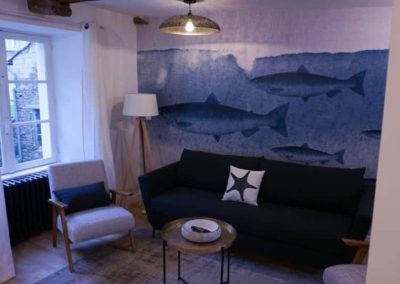 Salon avec canapé noir, fresque de poissons et fauteuil scandinave