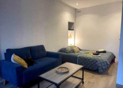 Lit double avec housse de couette à motif tropical, meuble TV et déco minimaliste.