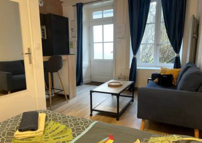 Pièce principale avec canapé bleu, lit double et éclairage d’ambiance.